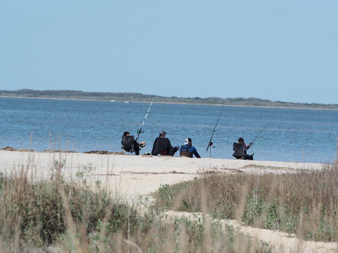 Three people sitting in chairs while holding fishing poles.