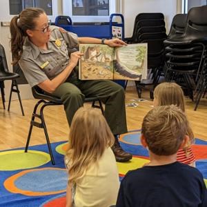 A park ranger reading a book to a group of kids.