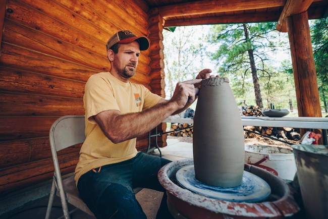 Artist-in-Residence Brad Bachmeier works with clay on a potters wheel on a cabin porch.