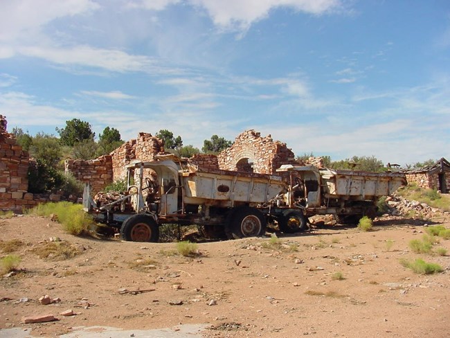 Old ore hauling trucks parked next to the red stone buildings that were once used for offices at Grand Gulch Mine.