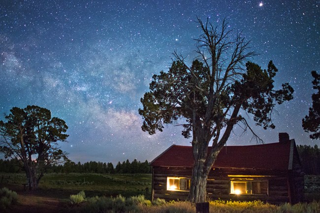 View of the night sky with thousands of stars. A cabin is seen beneath the night sky.