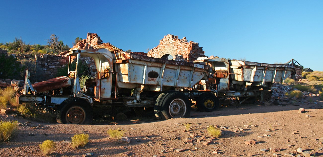 Two abandoned dump trucks in front of a ruin of a brick mine building