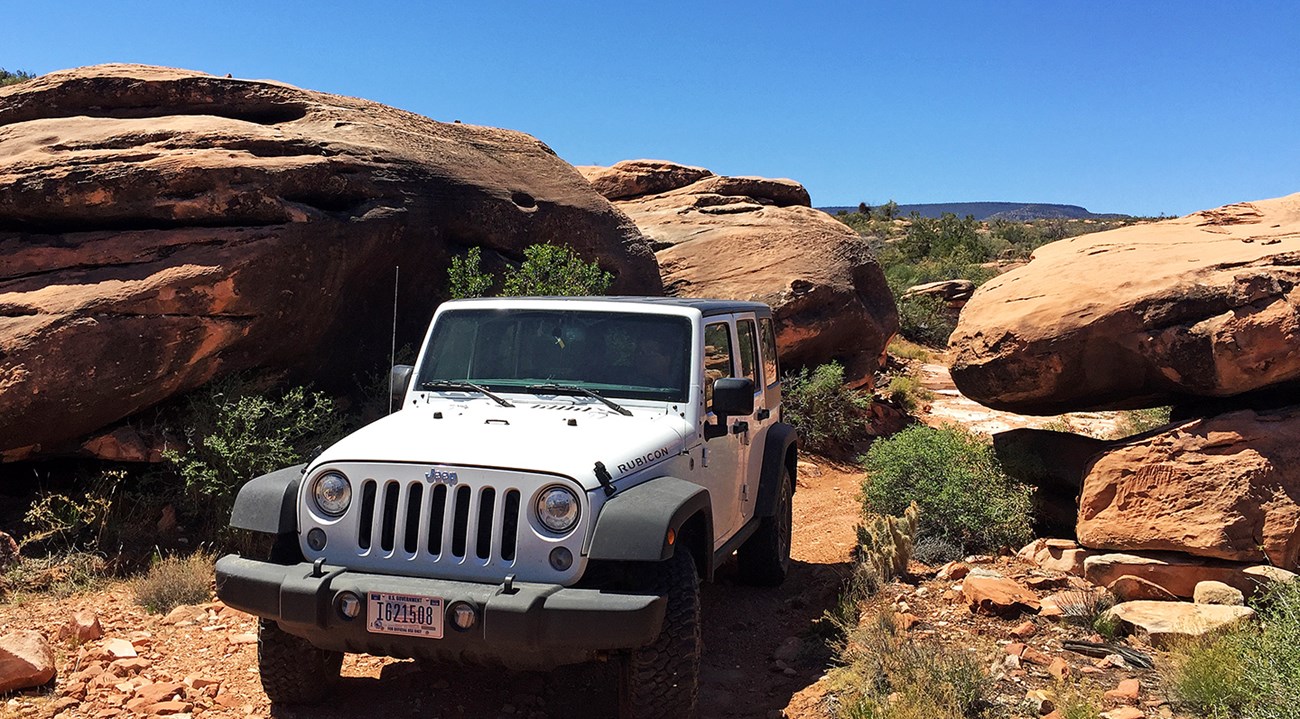 Jeep on narrow road between orange sandstone boulders