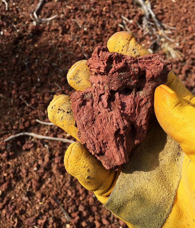 Red volcanic scoria in a gloved hand