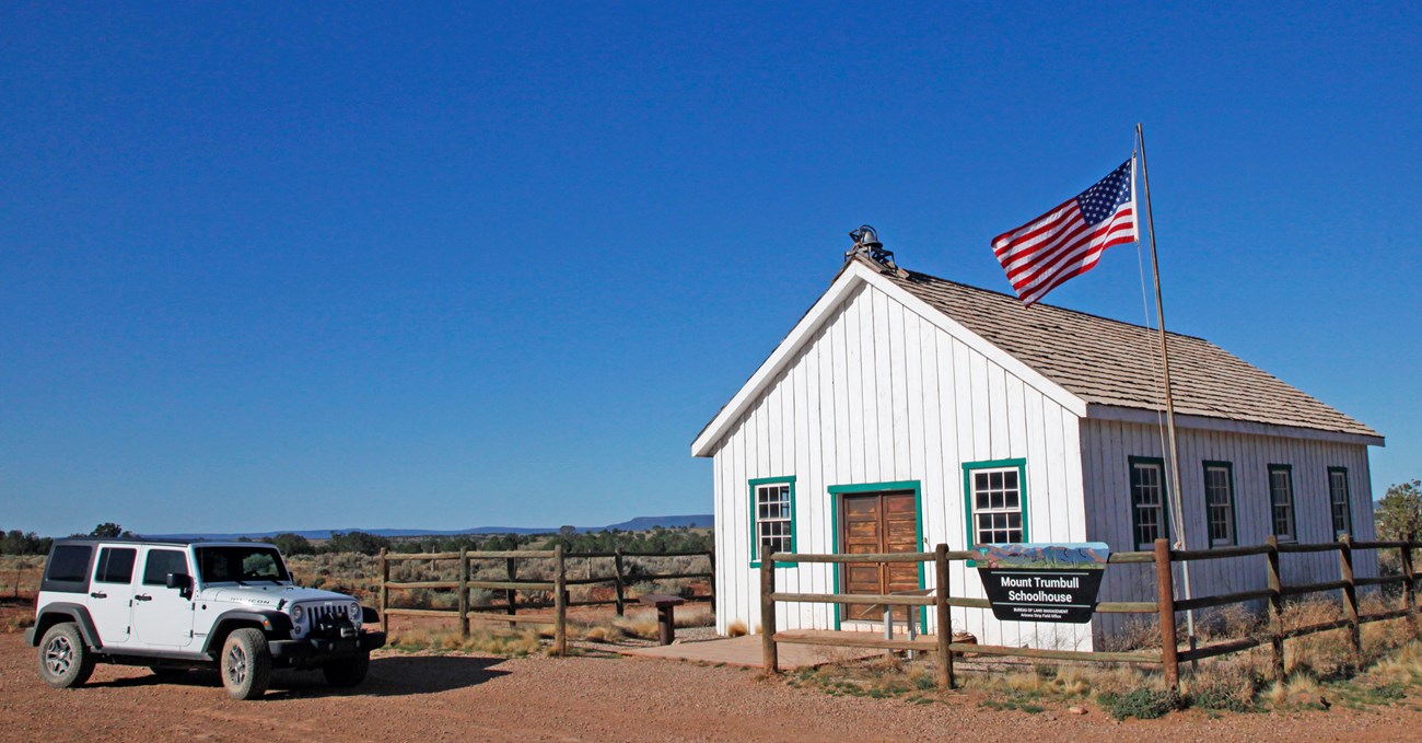Historic one room schoolhouse with American flag and Jeep parked outside