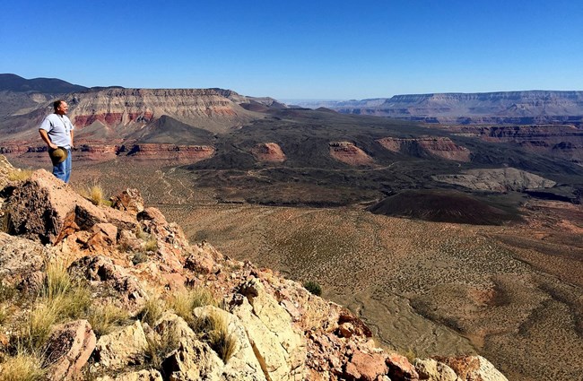 Person standing at Whitmore Point 2,000 feet above the valley looking south over the Grand Canyon and a giant lava flow into a valley