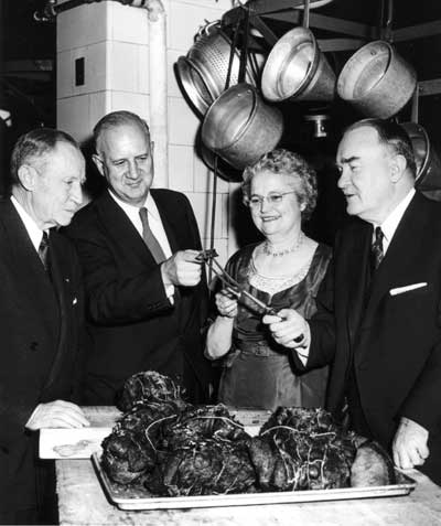 Mrs. Singer holding bison and elk meat with tong as Conrad Wirth, Clarence Davis, Russel Singer look on.