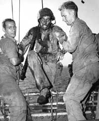 Coast Guardsmen assist a battle-blackened Marine on board
