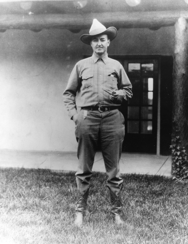 A man standing in front of a doorway wearing a cowboy hat.