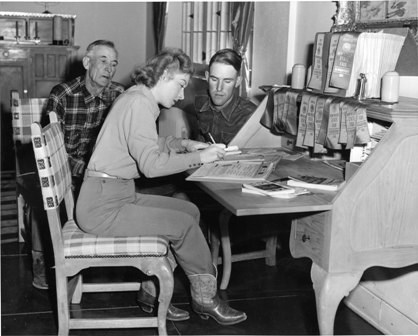 Woman signing documents at desk as two men look on