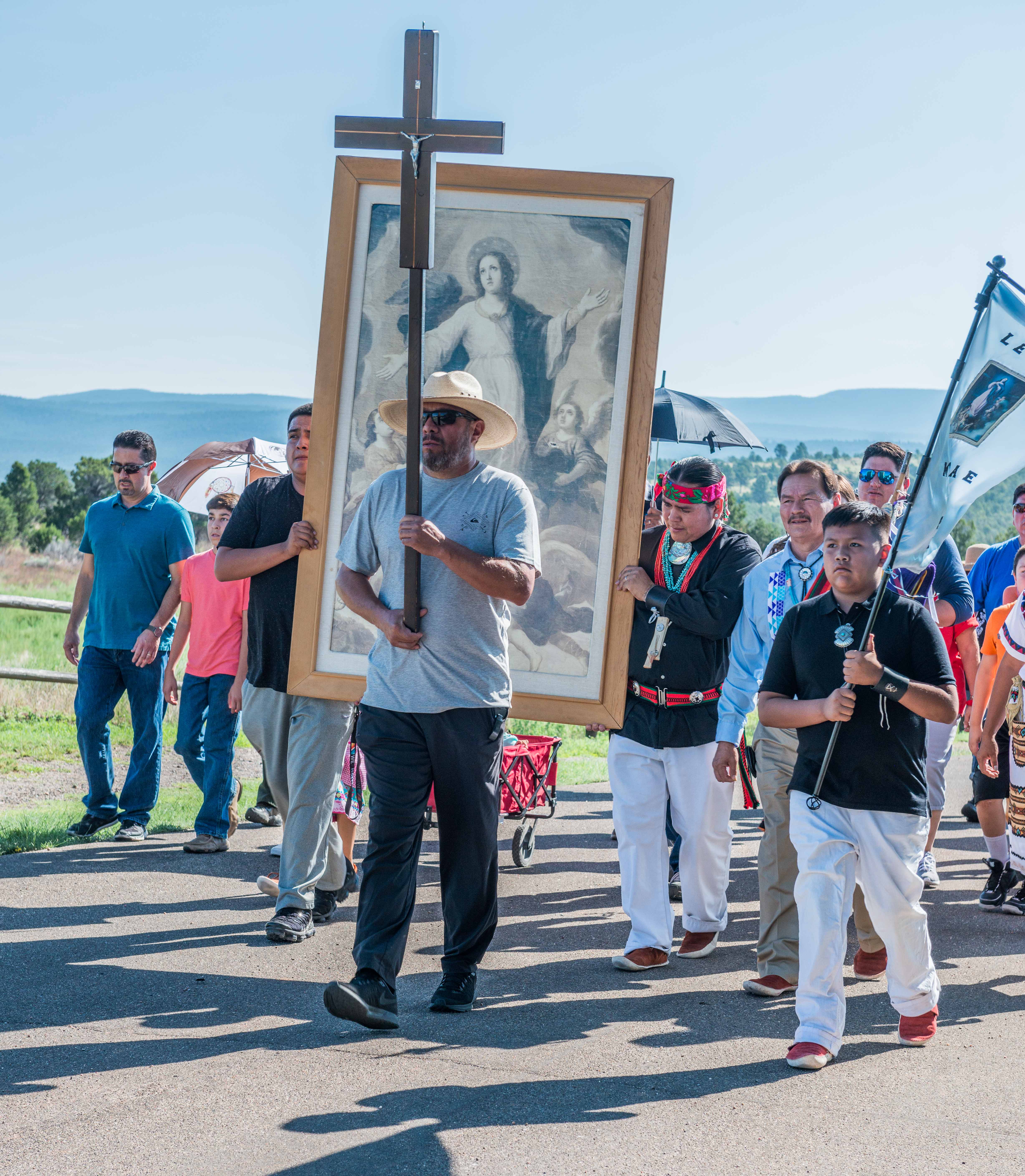 Procession of the 2018 Feast Day. People walking in a group with a picture and a cross.