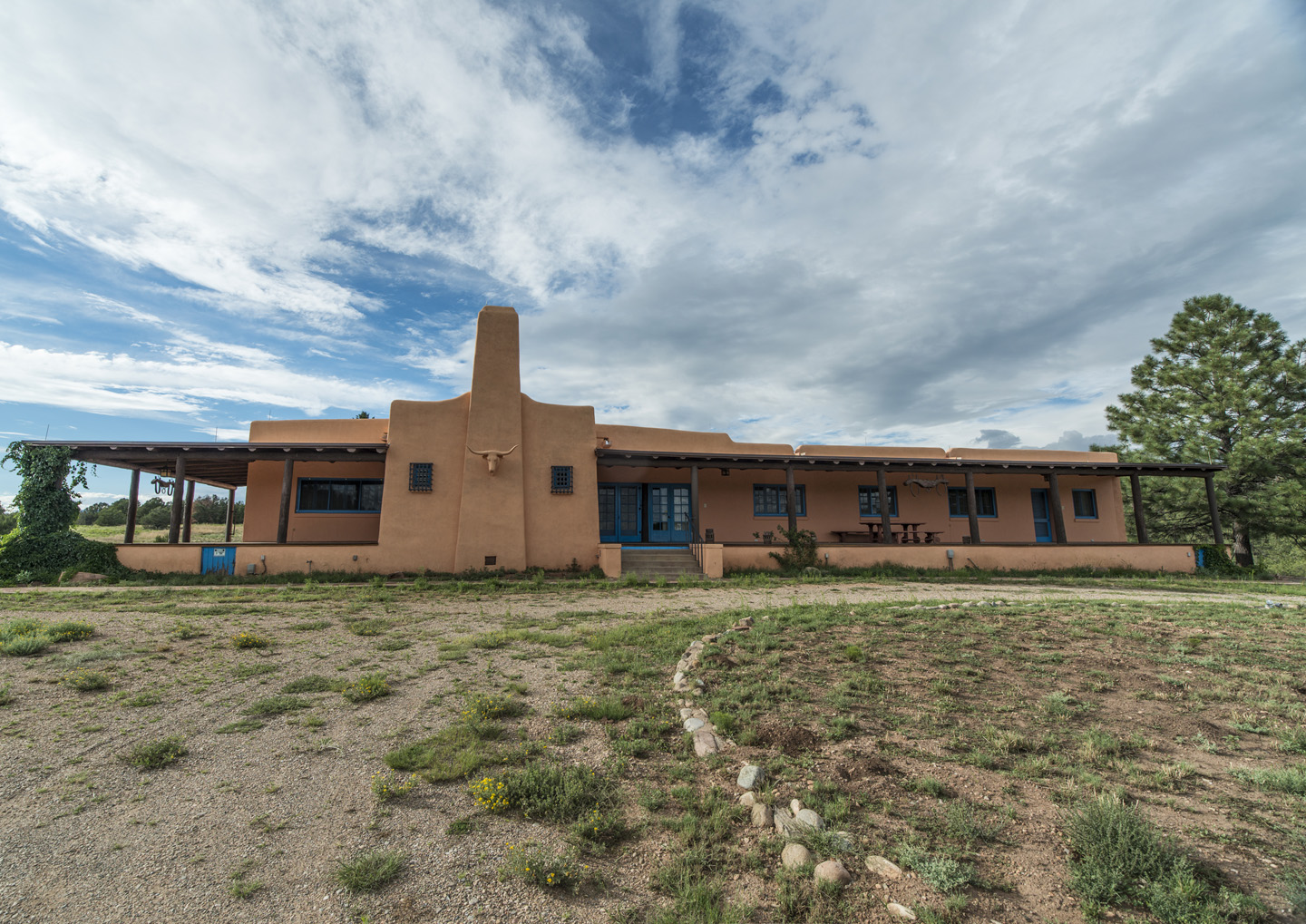 The Forked Lightning Ranch House A building with clouds in the background and grass in the foreground.