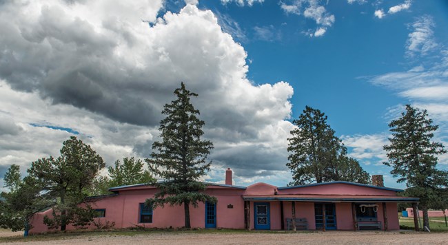A pink building surrounded by trees and a cloudy sky.