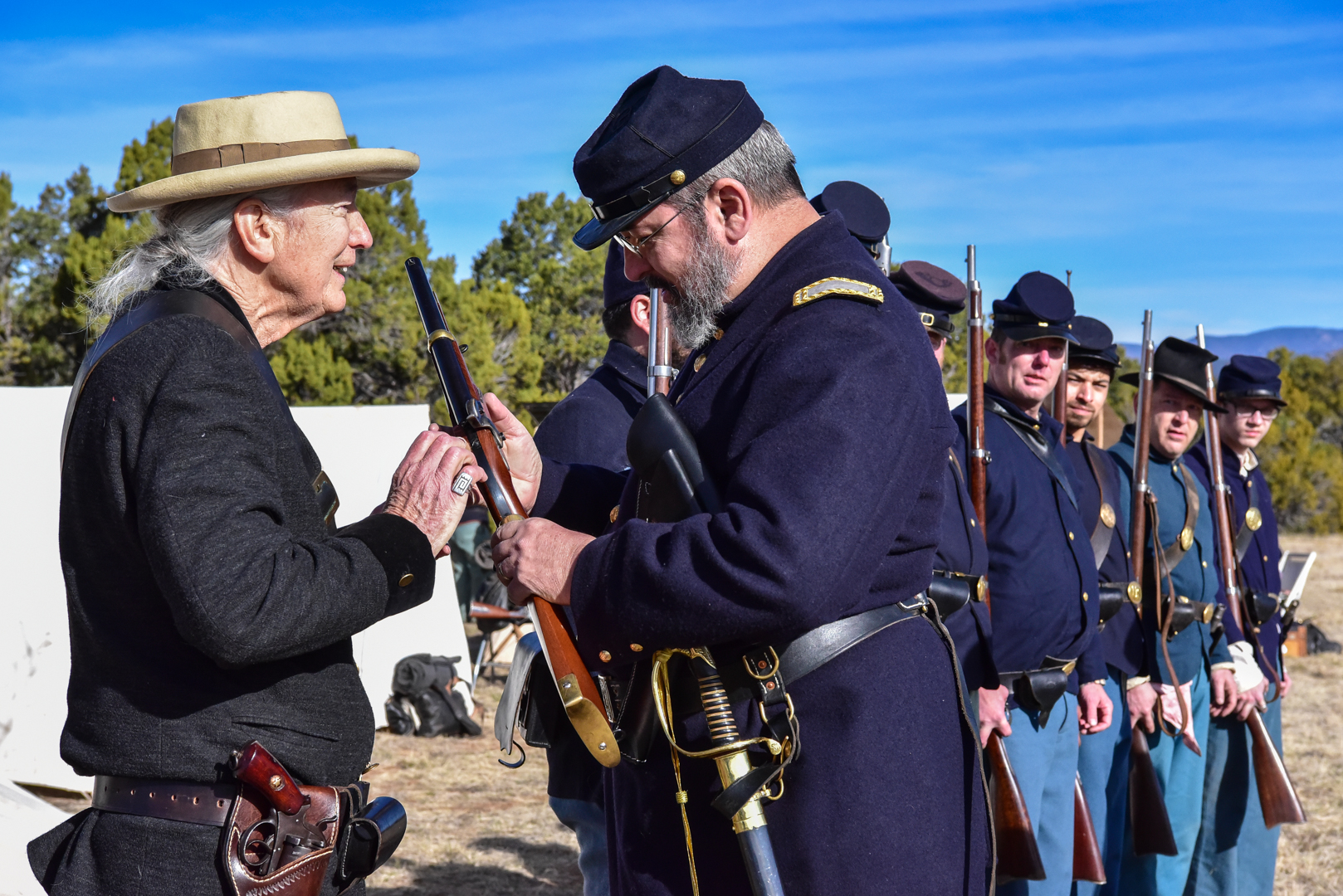 Men standing in a line dressed in period clothing holding period firearms.