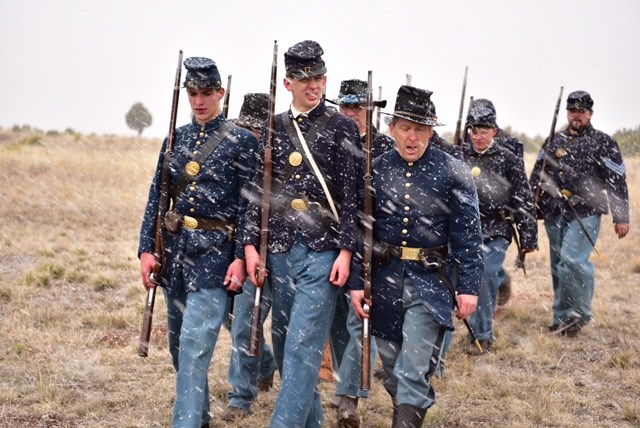 People marching in Civil War military uniforms marching in snow.