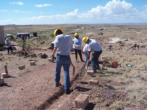 Youths in hard hats work with tools along a trail.