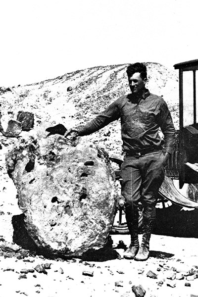old photo of man standing next to petrified wood and old car