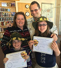 A family with 2 kids holding up Jr Ranger certificates A family with 2 kids holding up Jr Ranger certificates
