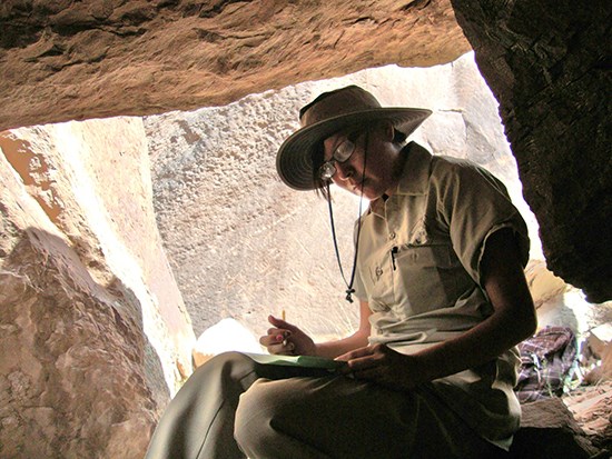 teen girl writes in notebook while sitting among rocks