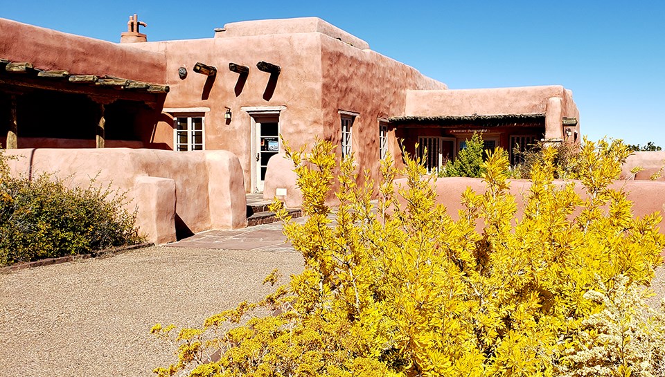 Pueblo style building beneath a blue sky with bright autumn foliage in front