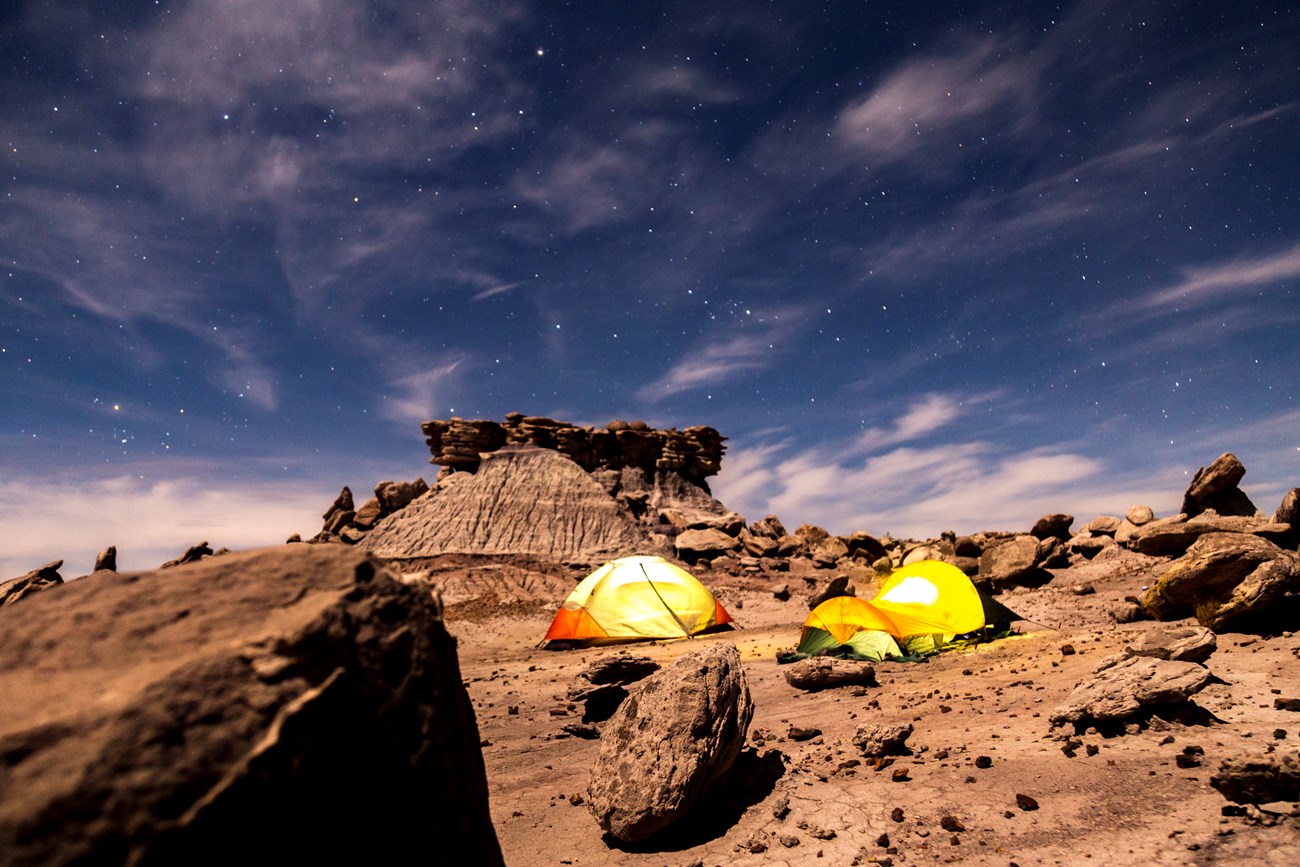 Two tents rest under starry skies among boulders and buttes in Devil's Playground.