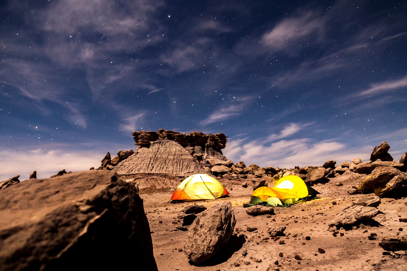 Camp Out at Devils Playground Two tents rest under starry skies among boulders and buttes in Devil's Playground.