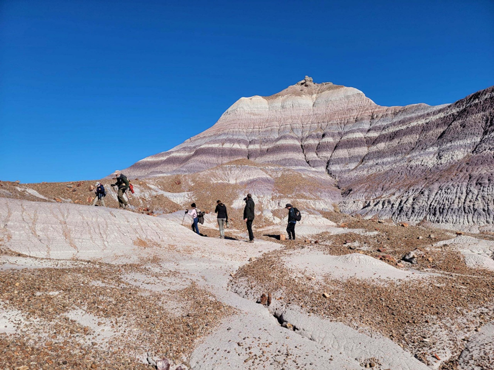 Visitors hiking in the Blue Forest area of the park. Visitors hiking in the Blue Forest area of the park, banded badlands under a very blue sky.