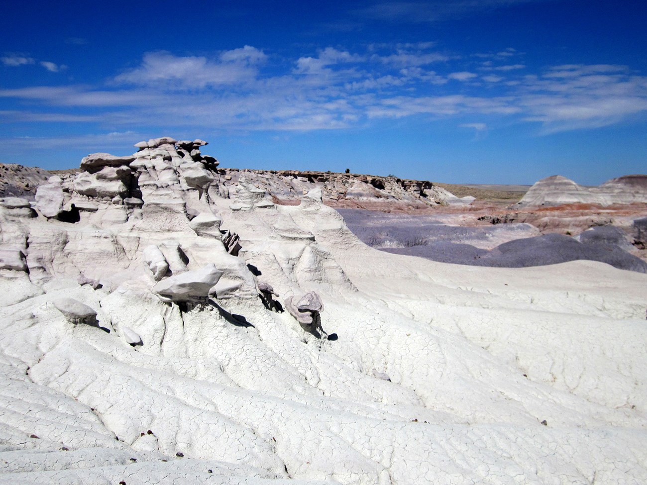 White geological formation called the Sandcastle with the colorful badlands in the distance of Red Basin under mostly blue sky.