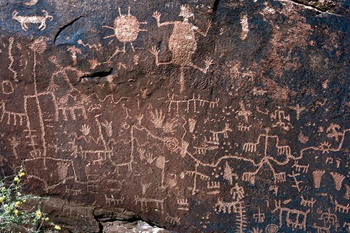 Lighter colored petroglyphs cover the dark brown surface of Newspaper Rock
