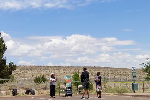 1st Amendment area: three people standing among trees and shrubs under a blue sky with white clouds.