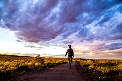 Hiker walks through grassland under sunset skies.