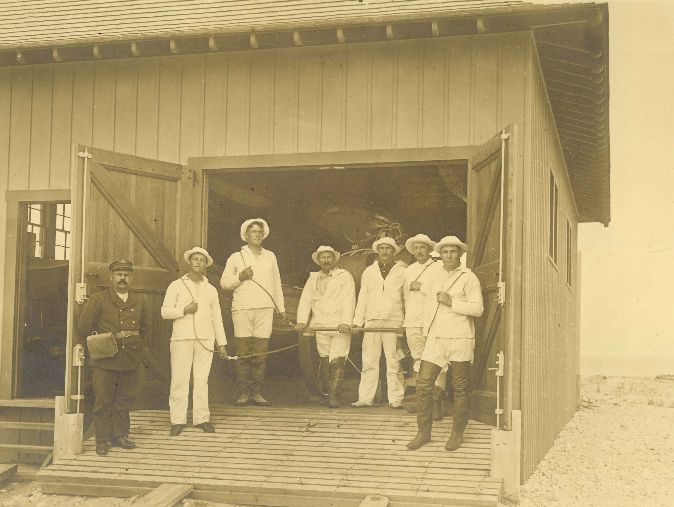 7 men stand in US Life Saving Service uniforms in the entrance to a building with a large garage