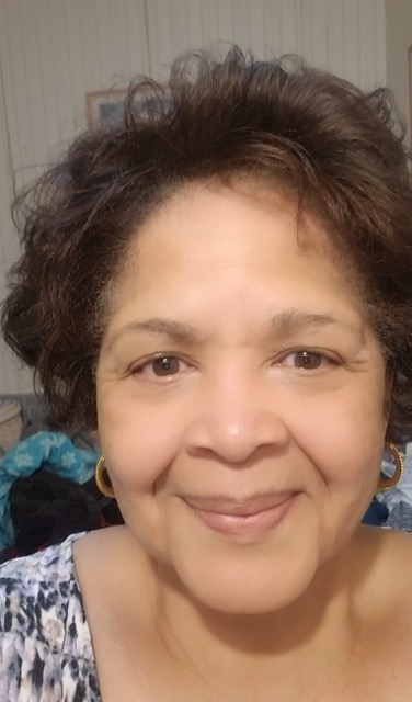 Headshot of a brown eyed brown hair woman with a slight smile and gold hoop earings.