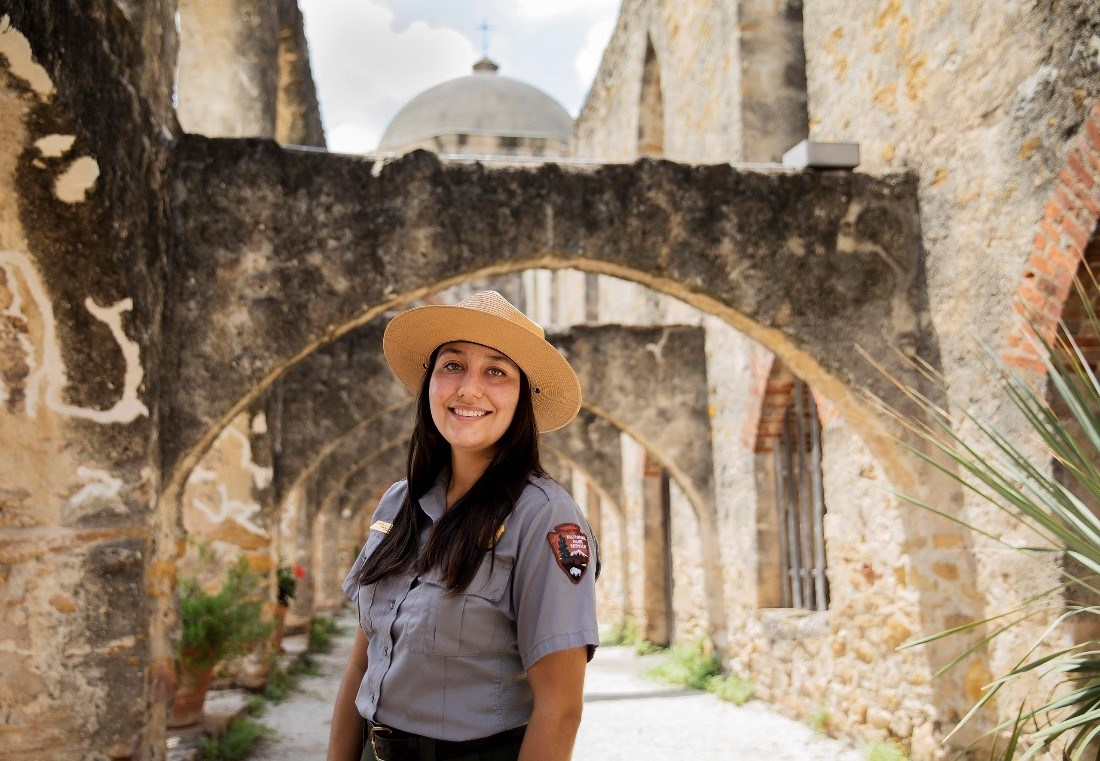 Woman smiling park ranger smiles under stone arches.