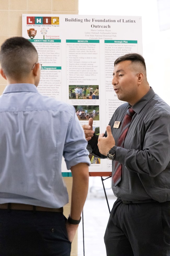MarioPresenting Two young men face each other. One is wearing professional attire and using hand gestures in front of a diagram