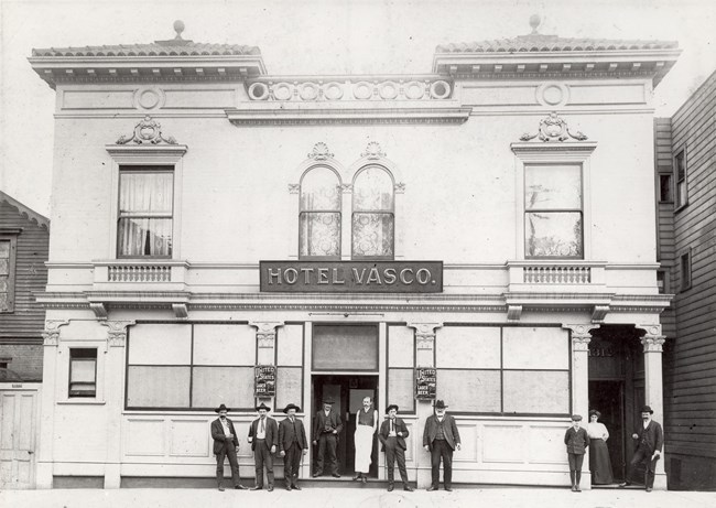 A black and white image of Hotel Vasco, operated by Martina Aguirre and her husband. Ten people stand in front of the hotel.
