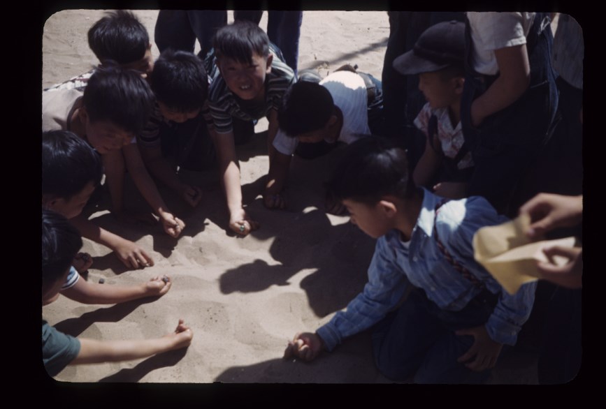 A group of kids playing with marbles on the ground. A group of kids playing with marbles on the ground.