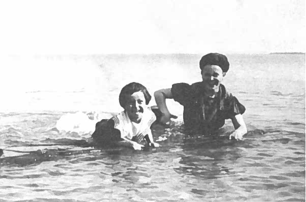 An adult and a child swim in a large body of water. They appear to laugh and play together, seemingly near shore.
