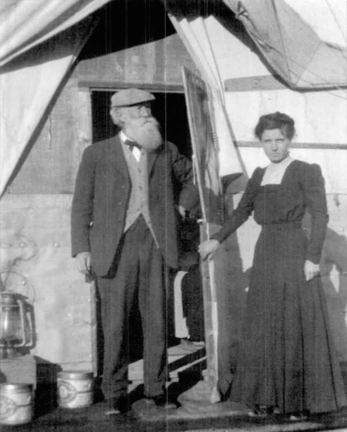 An old photo of Mary Beal with John Burroughs standing outside a tent home.