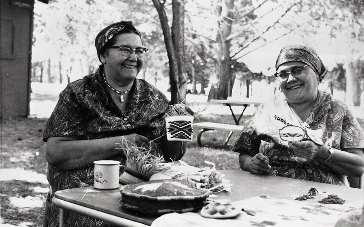 A black and white image of Ida Blackeagle and Viola Morris demonstrating beading and cornhusk weaving.