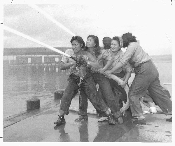 A black and white photo of Katherine Lowe and four other women training with fire hose, from left to right: Elizabeth Moku, Alice Cho, Katherine Lowe, and Hilda Van Gieson.
