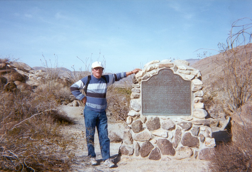Phil Valdez at Anza Borrego Desert State Park next to a California Historical Marker titled Santa Catarina. Man standing in a desert next to a large stone historical marker