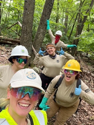 Trail crew A group of five individuals wearing hard hats pose stand outside in front of trees. Three are holding up their hands with their thumbs ups.