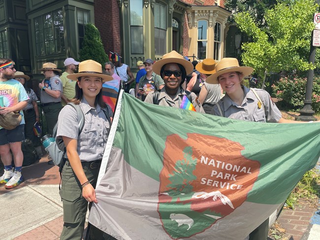 Three females hold a flag Three female National Park Service rangers hold NPS flag on a busy street