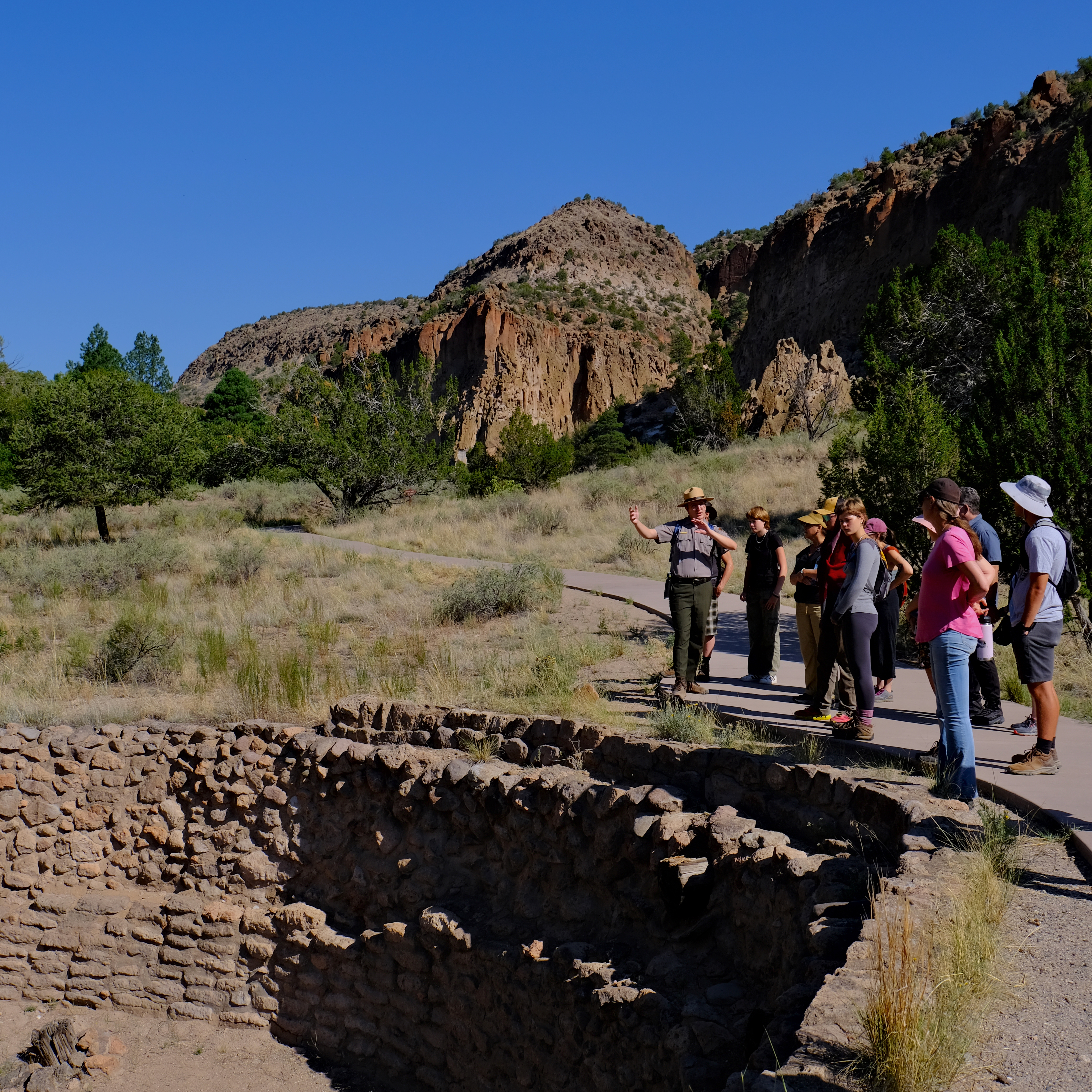 a ranger leads a group to a large excavated hole in the ground known as Big Kiva