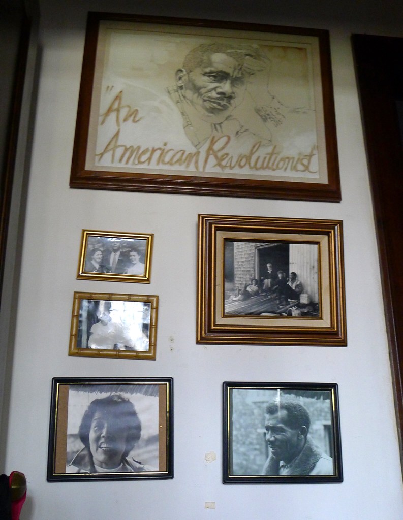 Wall of Photos at Grace Lee Boggs' Home, by On Being, 2011. Licensed under CC BY-NC-SA 2.0. James Boggs is at bottom right. Several framed photos mounted on a wall.