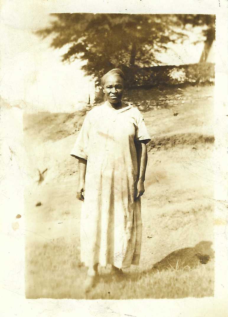 B&W photo of older black woman standing in a long white linen type dress for daily wear