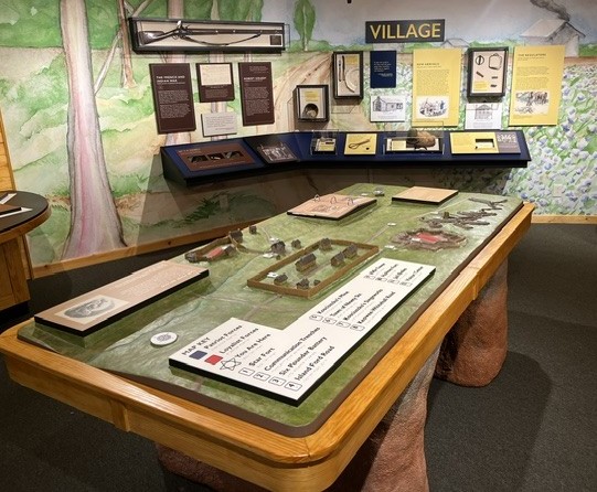 A museum with a table and a decorated wall showing mulitple displays and historical artifacts.