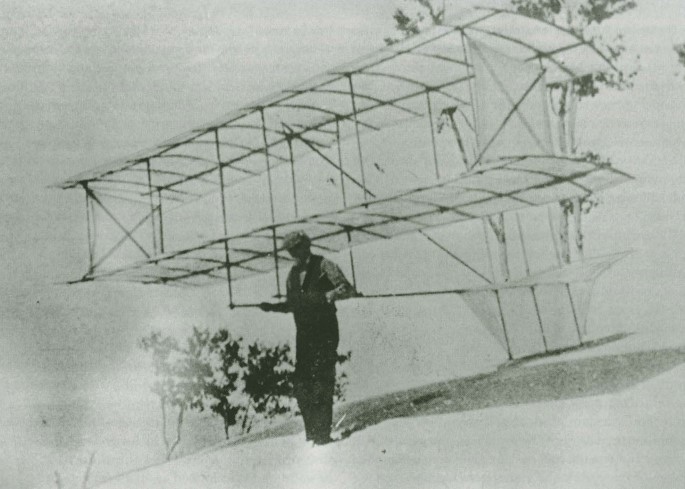 Black and white photograph of Octave Chanute standing on a sand dune holding his bi-wing glider.