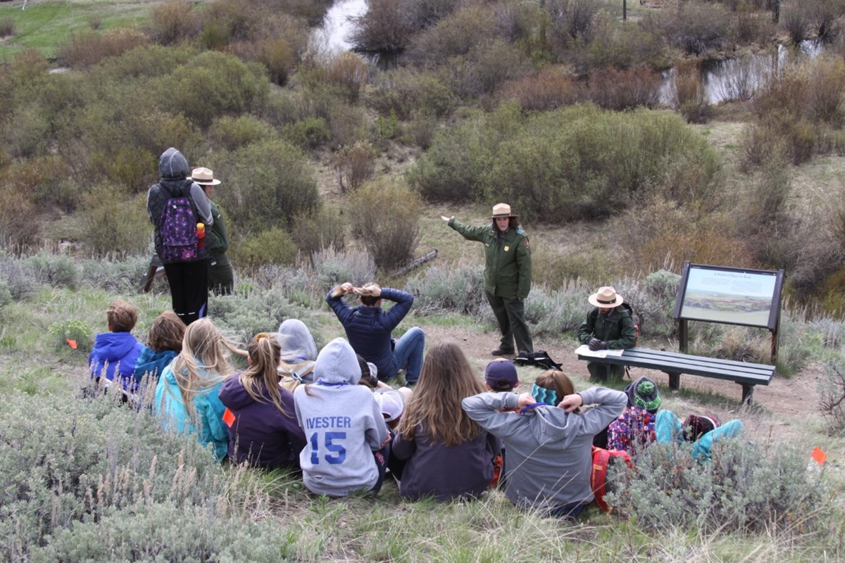 a female park ranger gives an outdoor presentation to visitors facing her